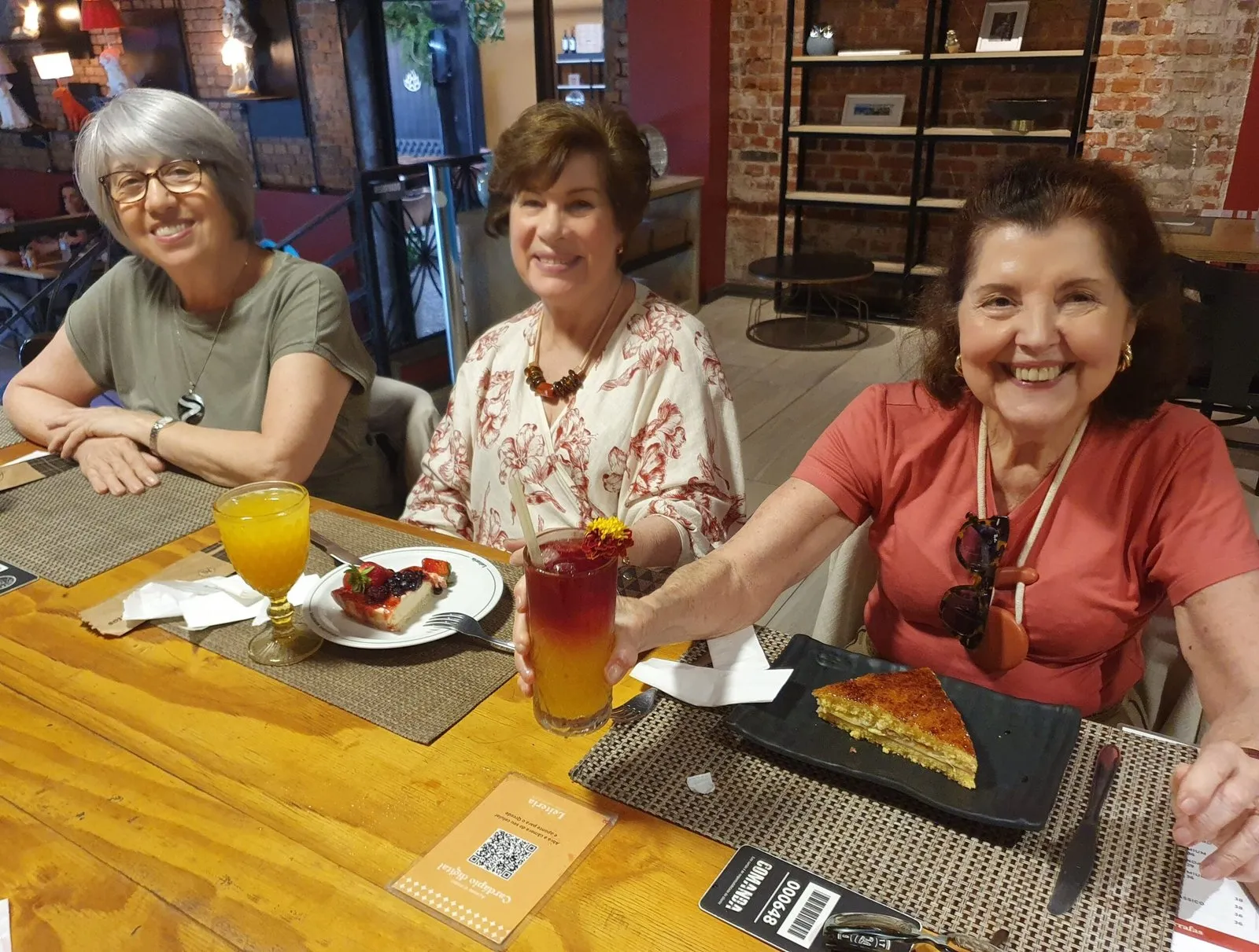 Três amigas da CICLOS+ sorriem à mesa, com lanches e bebidas