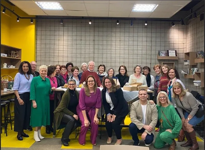 Grande grupo de alunas e alunos posa junto numa sala com parede amarela