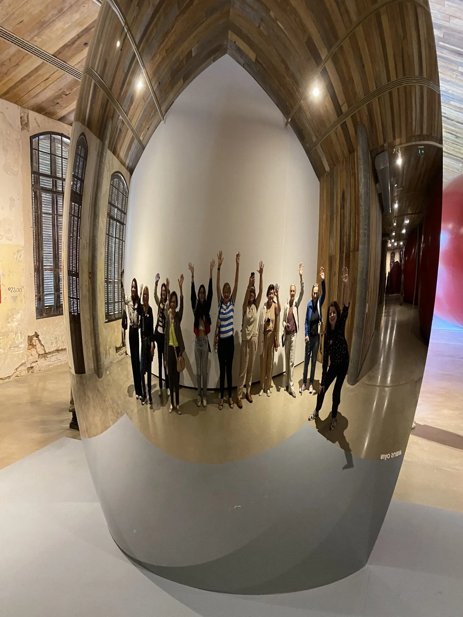 Grupo se diverte refletido numa grande escultura espelhada